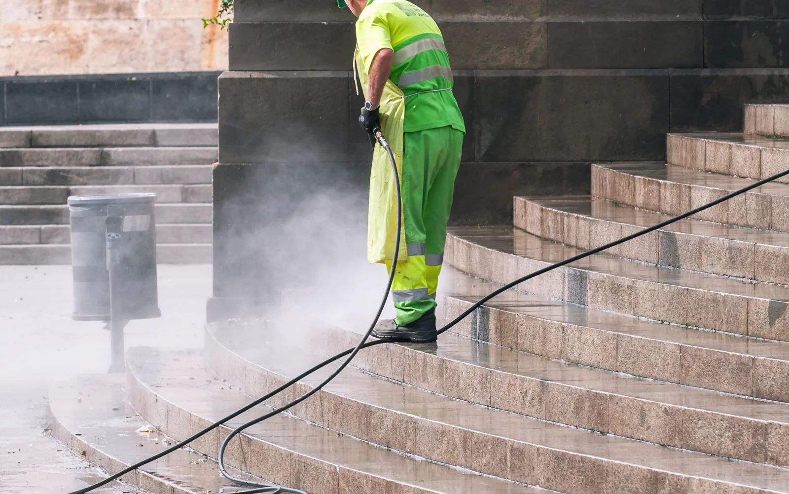 Exterior cleaning in progress on stone steps, water mist rising