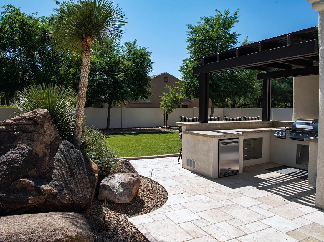 Paved outdoor entertaining area with an alfresco kitchen and palms